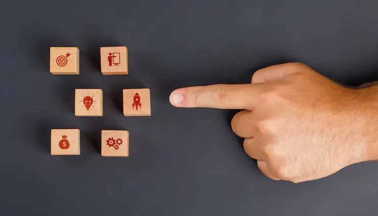 Finger pointing at wooden cube with business icon on grey table